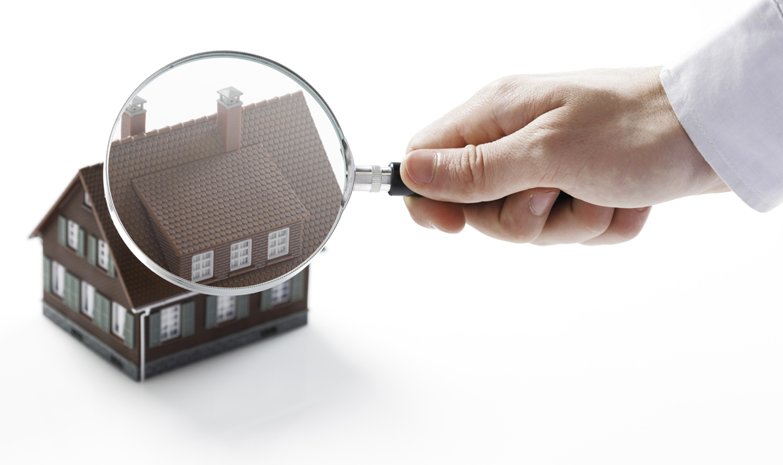 Hand holding magnifying glass over a model house, inspecting for property defects.