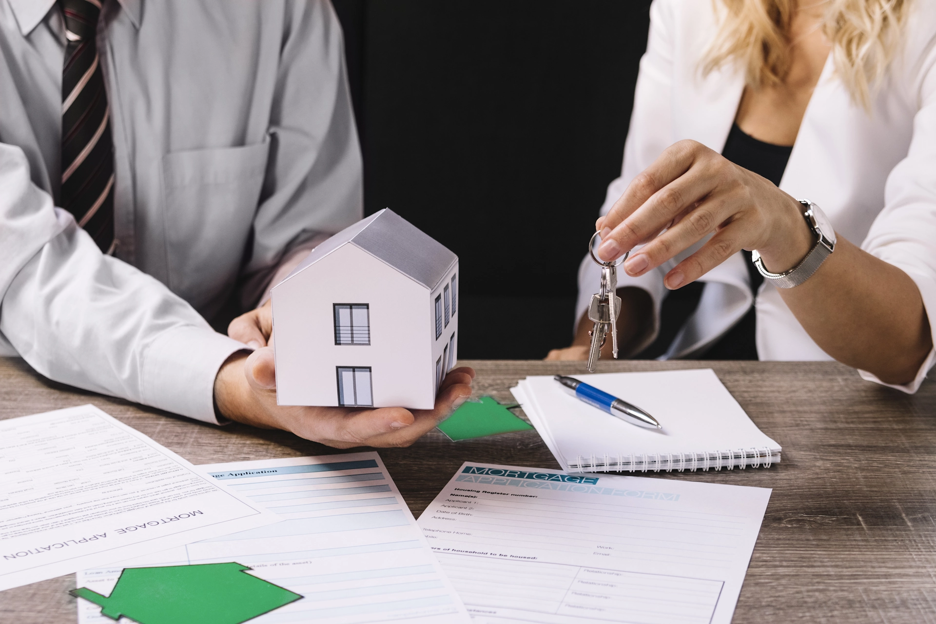 A mortgage broker and client shaking hands over a model house and keys, signifying a