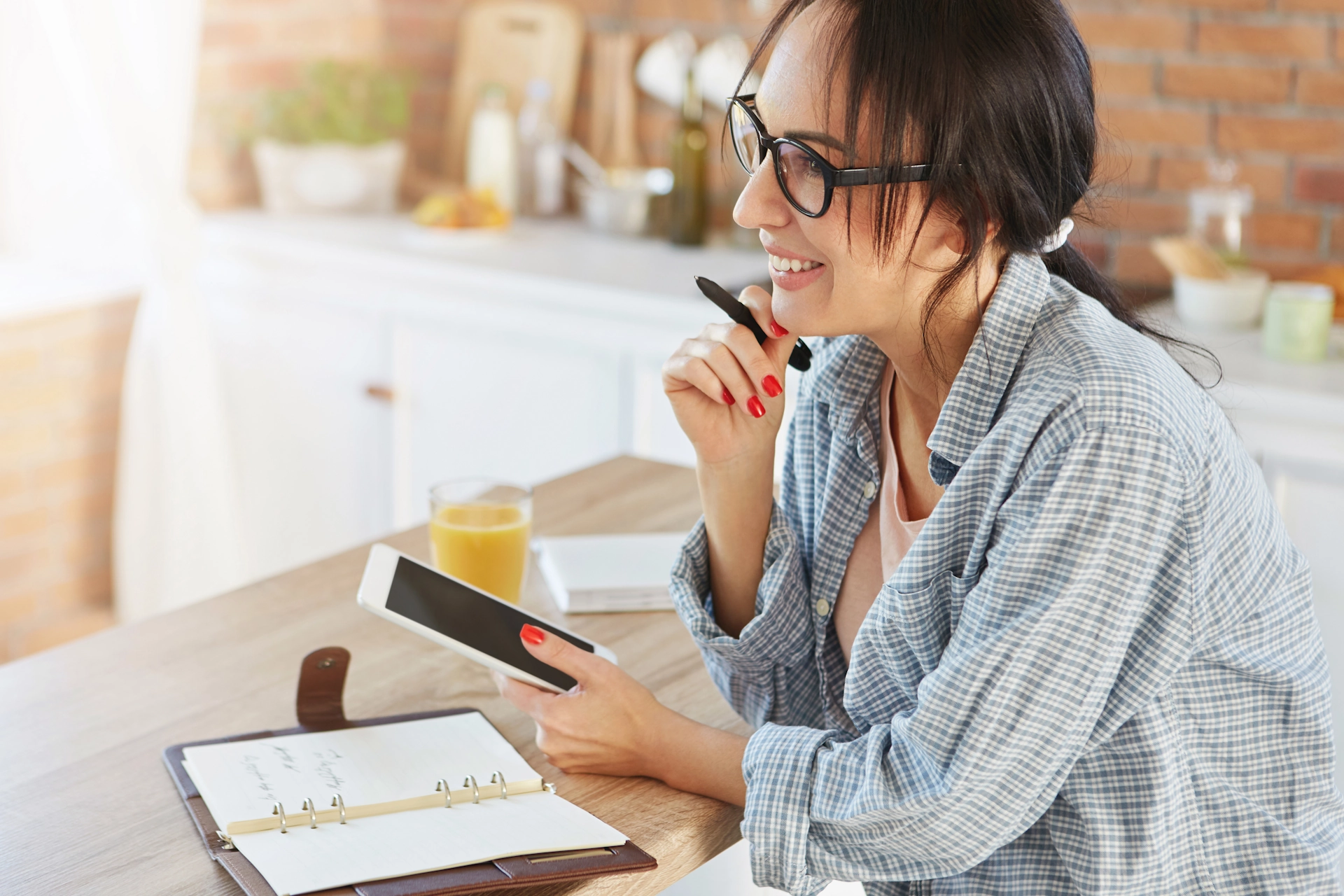 Woman using a tablet while reviewing financial documents in a modern kitchen setting.
