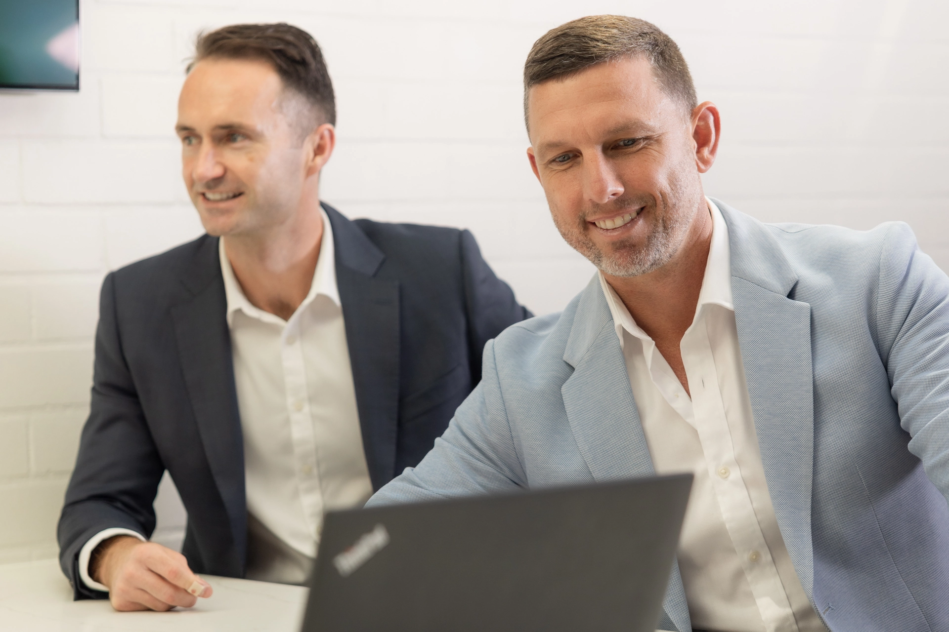 2 men in grey suits working on a laptop. business loan