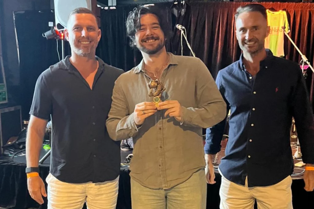 Three smiling men posing with a trophy at a Sutherland Shire event.