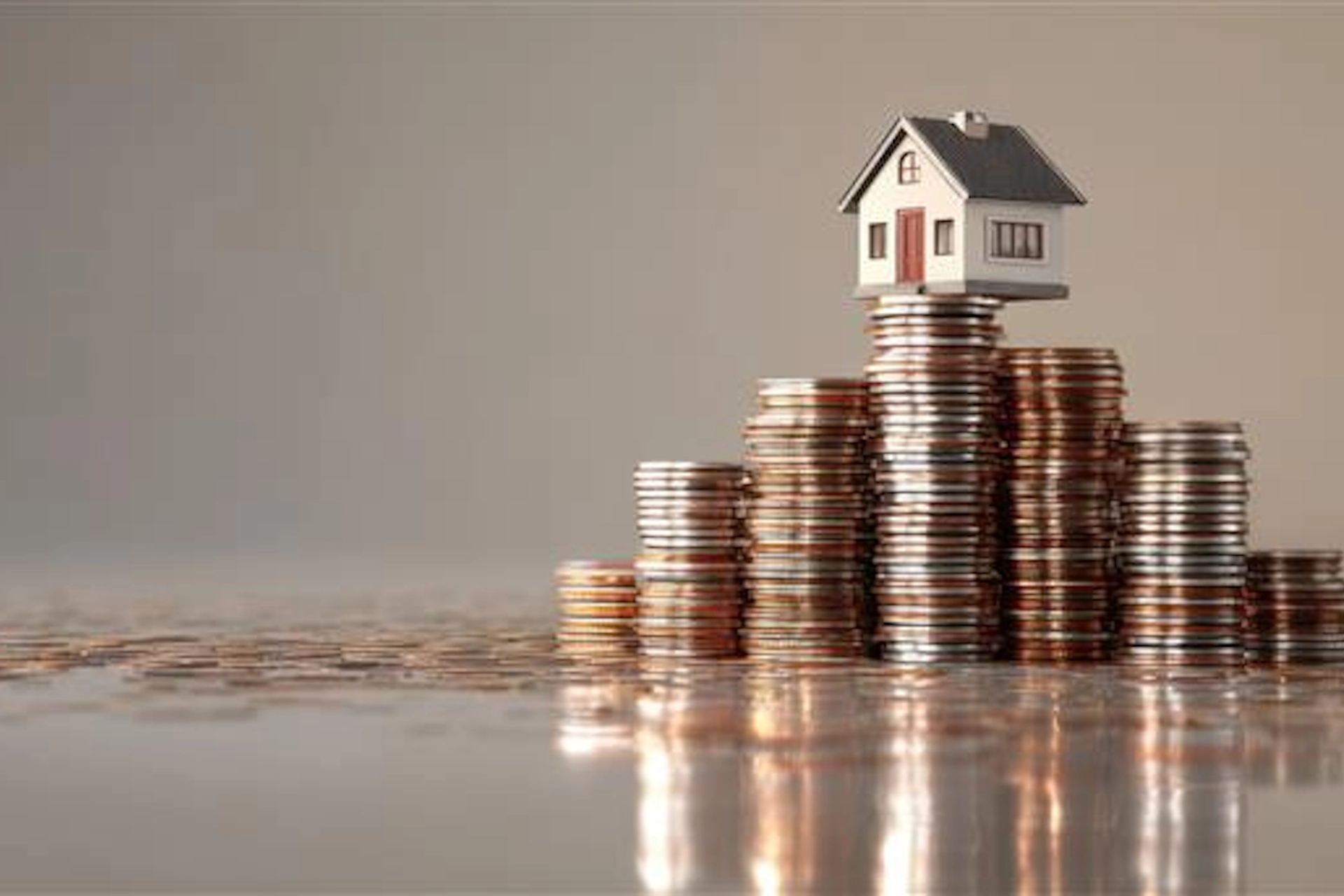 House model atop stacks of coins representing investment property loans and portfolio growth.