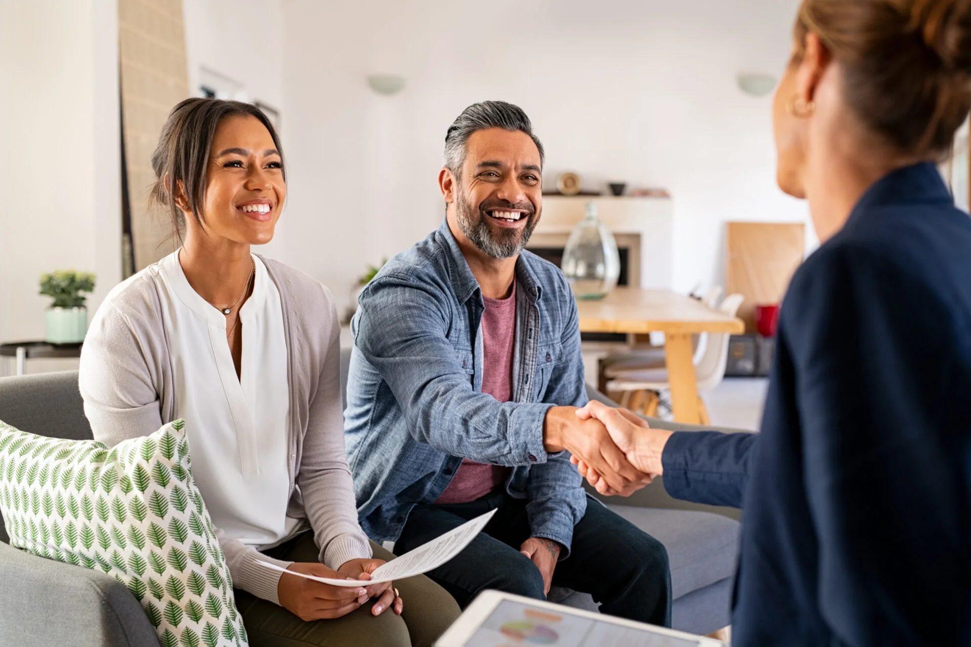 Couple smiling and shaking hands with a mortgage broker discussing first home buyer loans.