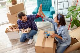 Couple celebrating new home purchase with moving boxes and plants nearby.