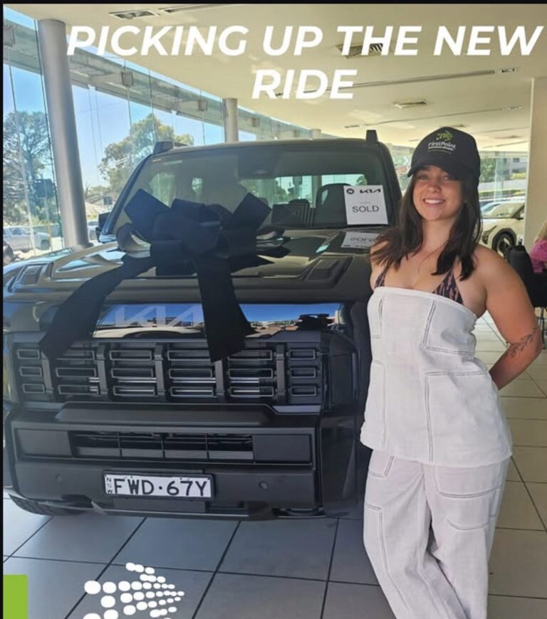 Happy customer standing with new car and large bow at a dealership in Australia.