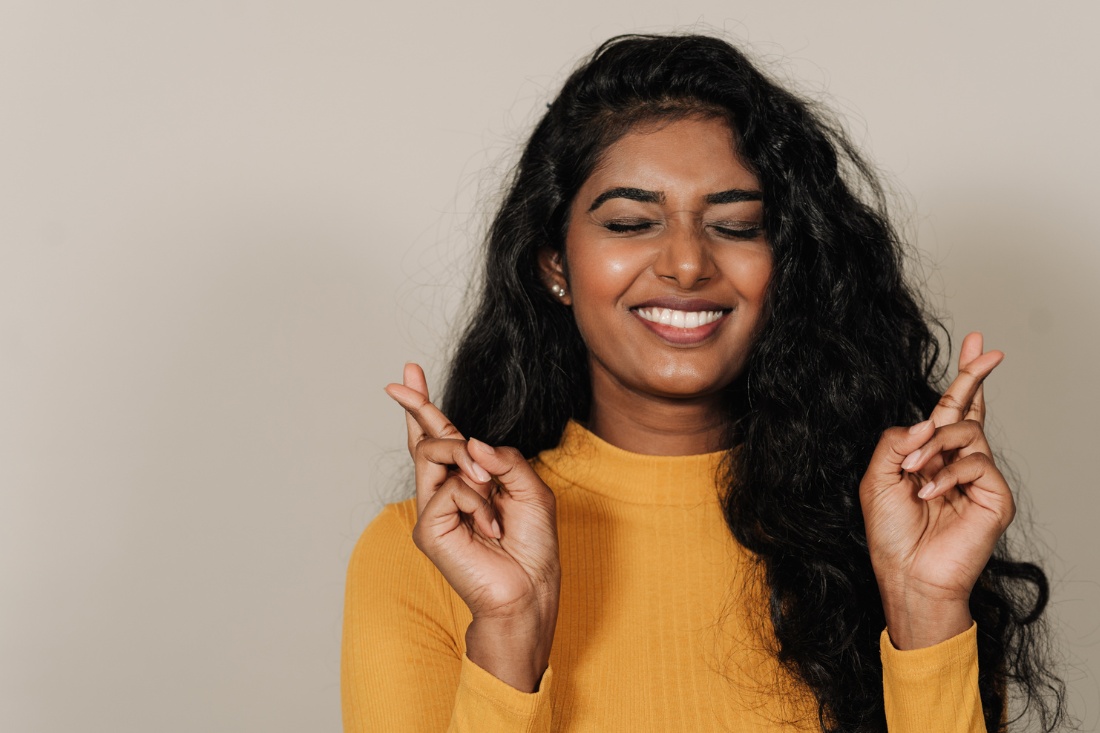 Woman with crossed fingers smiling, suggesting hope for first home buyers in Australia.